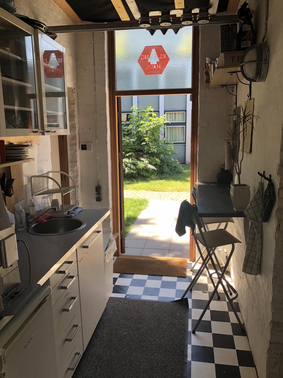 Fælleskøkkenet med KlangHaus' logo i dørglasset og åben dør til haven